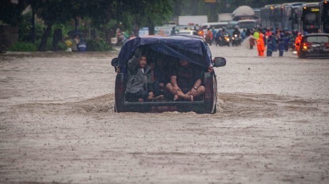 Warga menaiki mobil saat melintasi genangan banjir di Jalan DI Panjaitan, Cawang, Rabu (1/1/2020). Banjir tersebut disebabkan karena tingginya intensitas hujan yang mengguyur sejak Selasa (31/12/2019). (ANTARA FOTO/Aprillio Akbar)