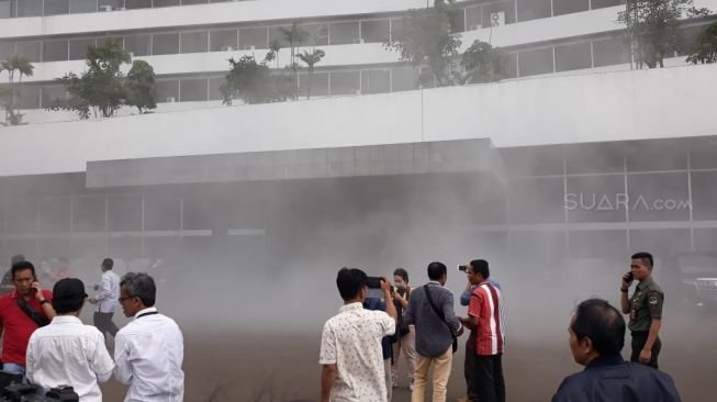 Pegawai dan pengunjung berada diluar Gedung Nusantara III DPR RI yang dipenuhi asap, Jakarta, Senin (24/2). [Suara.com/Novian]