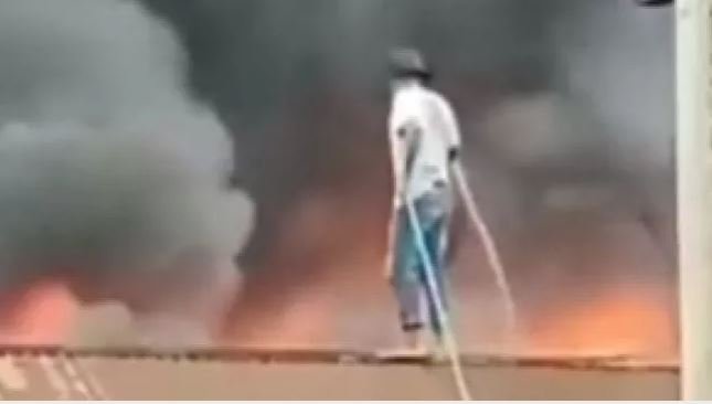 Seorang pria seorang diri menyiram kobaran api dari atas atap