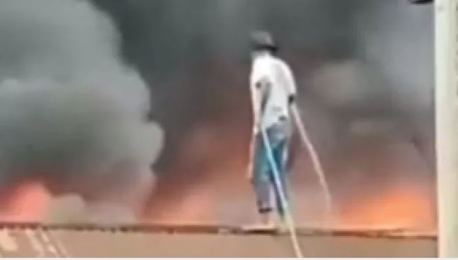 Seorang pria seorang diri menyiram kobaran api dari atas atap Seorang pria seorang diri menyiram kobaran api dari atas atap